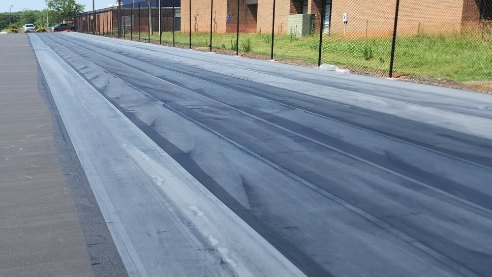 Crew installing Polypave across an asphalt tennis court