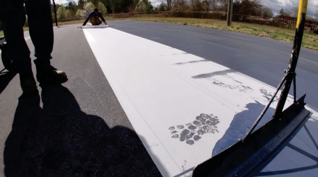 Crew installing Polypave across an asphalt tennis court